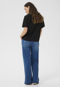 Camicia nera a maniche corte abbinata a jeans a gamba larga blu chiaro, con una texture liscia e una vestibilità casual, vista da dietro.