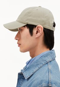 Casquette de baseball kaki avec une visière courbée, en tissu texturé et bandeau réglable à l'arrière, portée par une personne en veste en denim.