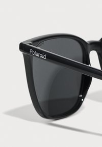 Black rectangular sunglasses with dark lenses. Features a shiny frame with "Polaroid" logo on the arm. Made of plastic material.