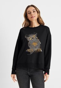 Zwarte sweatshirt met een grafisch ontwerp van een beer en "NEW YORK" in gouden en grijze accenten. Zachte textuur, losse pasvorm en ribbelmanchetten.