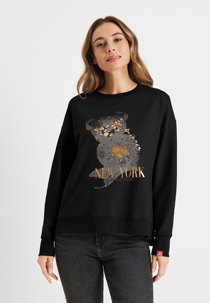 Zwarte sweatshirt met een grafisch ontwerp van een beer en "NEW YORK" in gouden en grijze accenten. Zachte textuur, losse pasvorm en ribbelmanchetten.
