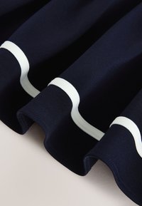 Marineblauer Stoff mit weichen Falten und weißen gebogenen Streifen nahe den Rändern, drapiert vor einer hellen Oberfläche.