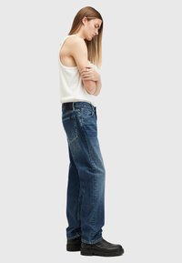 Jeans in denim blu a vita alta e svasati, con cinque tasche e una cintura nera. Abbinati a una canotta bianca e stivali neri alla caviglia.