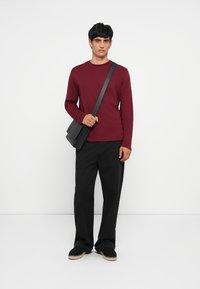 Maroon pikad varrukad särk, mustad püksid ja must ristisöömiseks mõeldud kott. Kingad on tumedad heleda tallaga. Minimalistlik disain, vabalt istuv.