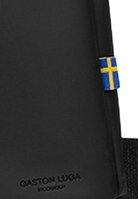 Zaino nero con una texture liscia, dotato di una piccola toppa con la bandiera svedese e "GASTON LUGA" impresso nella parte inferiore.