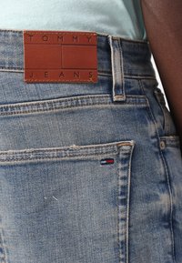 Denim teksad, millel on pleekinud sinine värv, nahast vöökohamärk "TOMMY JEANS" ja väike kolmevärviline aktsent tagakotil.