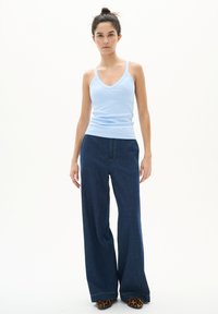 Débardeur côtelé bleu clair à bretelles spaghetti, associé à un pantalon en denim foncé à jambes larges avec des coutures visibles et une coupe classique.