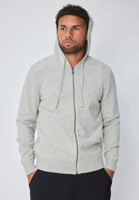 Sweat à capuche gris clair avec fermeture éclair, doté d'une capuche, fabriqué en tissu doux. Comprend des cordons de serrage, des poignets côtelés et une coupe ajustée. Sans motifs ni accents.