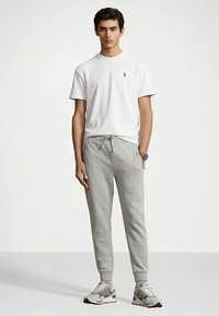 Vit bomulls t-shirt med en liten logotyp, kombinerad med ljusgrå sweatpants med dragsko. Modellen bär grå och vita träningsskor.