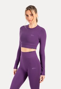 Paarse langmouwige cropped top met ronde hals en logo-detail, gecombineerd met hoge taille paarse leggings, gemaakt van rekbaar materiaal.