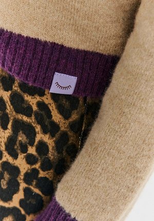 Knitted sweater featuring a beige body, purple ribbed hem, and leopard print accents. Includes a small lavender label with a graphic detail.
