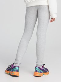 Leggings grigi in cotone con una texture liscia e una vestibilità affusolata, abbinati a scarpe sportive viola e turchesi con suole arancioni.