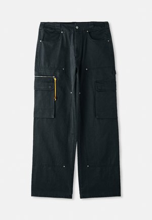 Μαύρο cargo παντελόνι φτιαγμένο από χοντρό ύφασμα, με άνετη εφαρμογή, πολλαπλές τσέπες, κίτρινη λεπτομέρεια στο φερμουάρ και μεταλλικά ασημί στοιχεία.