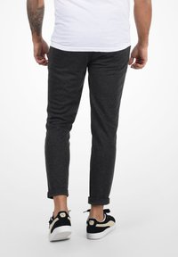 Pantalones gris ajustados con una textura suave, con puños enrollados, combinados con deportivas negras que tienen un acento beige y suela blanca.