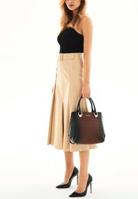 Black and brown croc-embossed handbag with gold hardware, featuring a structured design. Worn with a beige skirt and black high heels.