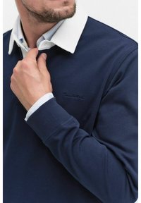 Marinblå tröja med vit krage, med ribbade manschetter och en diskret broderad logga på bröstet; bomullsblandning, slät textur.