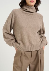 Vajas turtleneck pulóver, puha kötött anyagból, bordás mandzsettákkal és derékkal, magasan szabott vajas nadrággal párosítva.