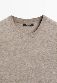 Krémový pletený svetr s kulatým výstřihem. Má hladkou texturu a ribbed manžety. Štítek zobrazuje název značky "Massimo Dutti."