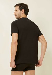 Black short-sleeve t-shirt with a round neck. Smooth texture, casual design. Worn with black shorts, visible from the back view.