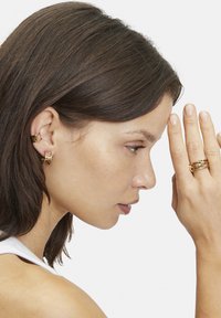 Bijoux dorés avec un crochet d'oreille géométrique et des bagues superposées. Texture lisse avec une finition polie ; design minimaliste et moderne.