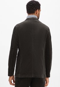 Dunkelgraue Cordjacke mit strukturierter Oberfläche, mit Kragen, langen Ärmeln und geradem Schnitt. Enthält seitliche Taschen.