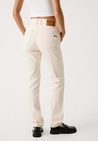 Jeans slim-fit color crema con etichetta in pelle, "Red Bull Racing x Pepe Jeans", e dettagli ricamati rossi sulla tasca posteriore.