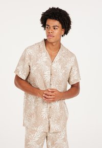 Camisa de botones de manga corta en color beige con estampado de hojas blancas, hecha de tela ligera, con un corte relajado y un cuello con muesca.