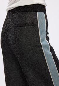 Pantalons noirs avec une texture brillante, ornés d'une fine bande latérale bleu clair et d'une petite poche arrière pour le détail. Ceinture élastiquée.