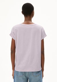 T-shirt lavanda a maniche corte con maniche arrotolate e scollatura rotonda, abbinata a jeans in denim azzurro chiaro. Materiale in cotone morbido.