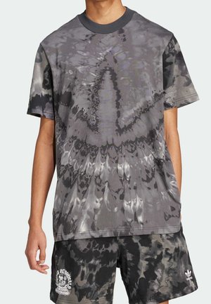 Graues Batik-T-Shirt mit einem runden schwarzen Halsausschnitt, das ein wirbelndes Muster zeigt. Kombiniert mit schwarzen Shorts, die weißen Text und ein Logo zeigen.