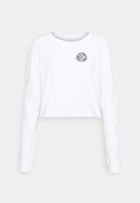 Vit långärmad crop-top t-shirt i bomull, med en cirkulär svart Nike-logotyp på framsidan, rund halsringning och avslappnad passform.