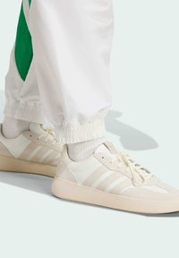 Bijele tenisice s glatkim kožnim gornjim dijelom, s tri horizontalne pruge, vezanjem na vezice i svijetlim gumenim potplatom.