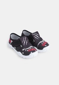 Chaussures noires pour enfants avec un design de griffes de dinosaure, une semelle en caoutchouc blanche et une sangle Velcro. Accentuées par le lettrage rouge "DANGER".