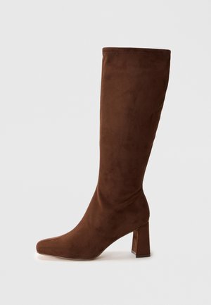 Bottes brunes en daim hauteur genou avec un bout carré et un talon épais. Texture lisse et design ajusté, avec un bord sans couture en haut.