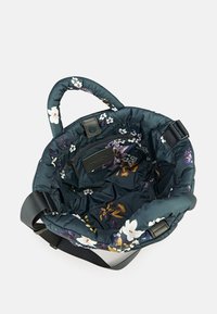 Sac cabas matelassé à motif floral foncé, doté d'un intérieur doux, de poignées courtes et d'une bandoulière ajustable. Contient une poche zippée.
