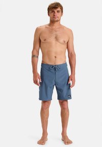 Kék úszónadrág, húzózsinóros derékrésszel, világosabb kék oldalsávokkal és fekete márkajelzéssel az alsó lábszáron. Könnyű anyagból készült.