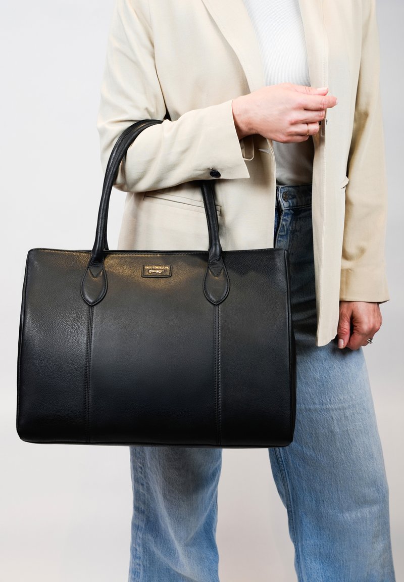 Zwarte leren tote bag met twee handvatten, voorzien van een soepele textuur, subtiele stiksels en een klein metalen logo-plaatje aan de voorkant.