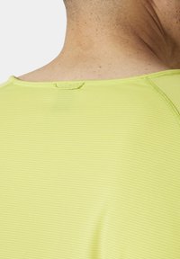Jasnożółta koszulka sportowa z teksturowanym, prążkowanym wzorem, z okrągłym dekoltem i pętelką na plecach do zawieszenia.