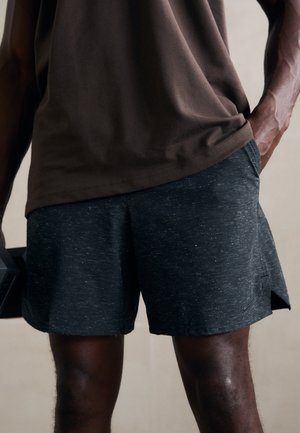 Shorts de sport noirs avec un motif discret de taches, fabriqués dans un tissu léger. Poches latérales et une légère fente à l'ourlet sont présents.
