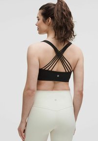 Sostenedor deportivo negro con tirantes cruzados, que resalta una textura suave. Combinado con leggings de talle alto de color claro.