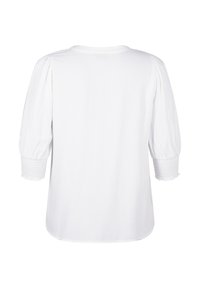 Blouse blanche à manches bouffantes trois-quarts et poignets smockés, avec une texture lisse et un ourlet arrondi.