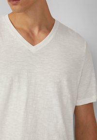 Witte v-hals t-shirt van lichtgewicht, gemêleerd stof met korte mouwen. Heeft een relaxte pasvorm en subtiele stikdetails langs de halslijn.