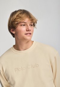 Felpa beige con vestibilità ampia, con un logo testurizzato "Polo Club" sul davanti. Collo e polsini a costine, tessuto morbido.