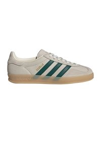 Αθλητικά παπούτσια Adidas Gazelle με επάνω μέρος από μπεζ σουέντ, πράσινες δερμάτινες λωρίδες και διαφανές σόλα από καουτσούκ καφέ. Χρυσές λεπτομέρειες με το λογότυπο.