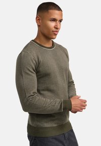 Pulover texturat de culoare verde măsliniu cu decolteu tip crew, manșete și tiv cu nervuri. Prezintă un model subtil, umeri fără cusături și un material moale.