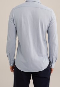 Světlomodrá košile s dlouhým rukávem, límcem na knoflíky a zakřiveným lemem. Vyrobena z texturované látky, disponuje manžetami na knoflíky a zadním dílem s vsadkou.