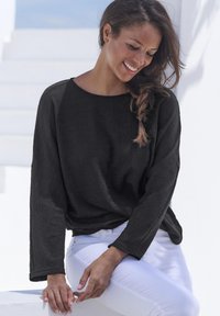 Top lungo nero a maniche, realizzato in tessuto testurizzato, con scollatura rotonda e vestibilità comoda, abbinato a pantaloni bianchi a vestibilità slim.