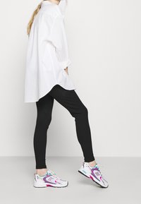 Vit skjorta med knappar och uppkavlade ärmar, svarta ribbade leggings och grå och rosa träningsskor med turkosa detaljer.