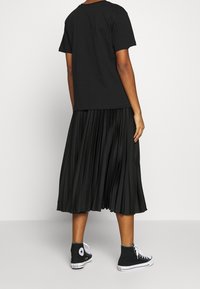 Camiseta negra, falda negra con pliegues y zapatillas altas negras. El conjunto presenta un ajuste holgado y una textura fluida en la tela.