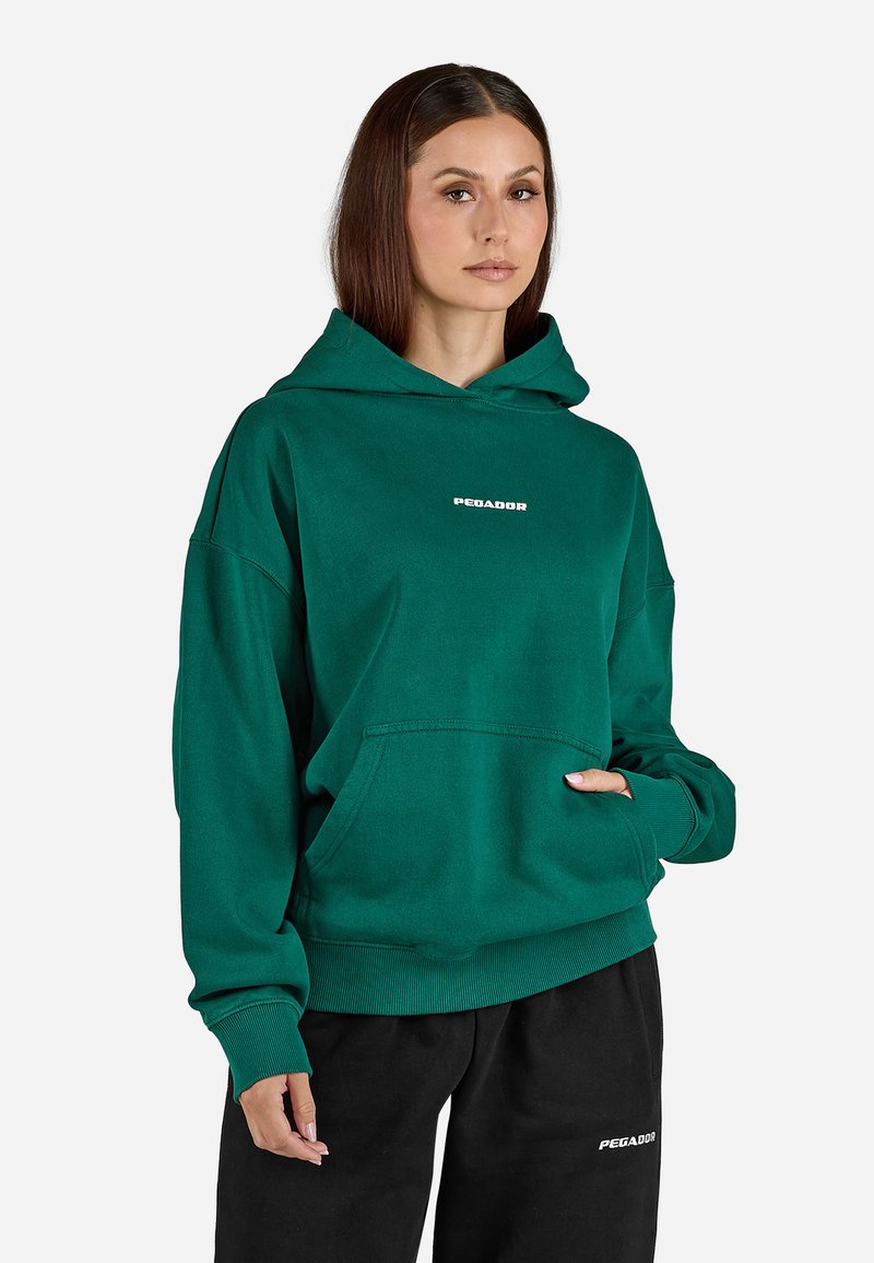 Sweatshirt verde com capuz, feito de algodão, apresentando um bolso frontal e punhos canelados. A parte da frente exibe um texto de logotipo branco. Combinado com calças pretas.